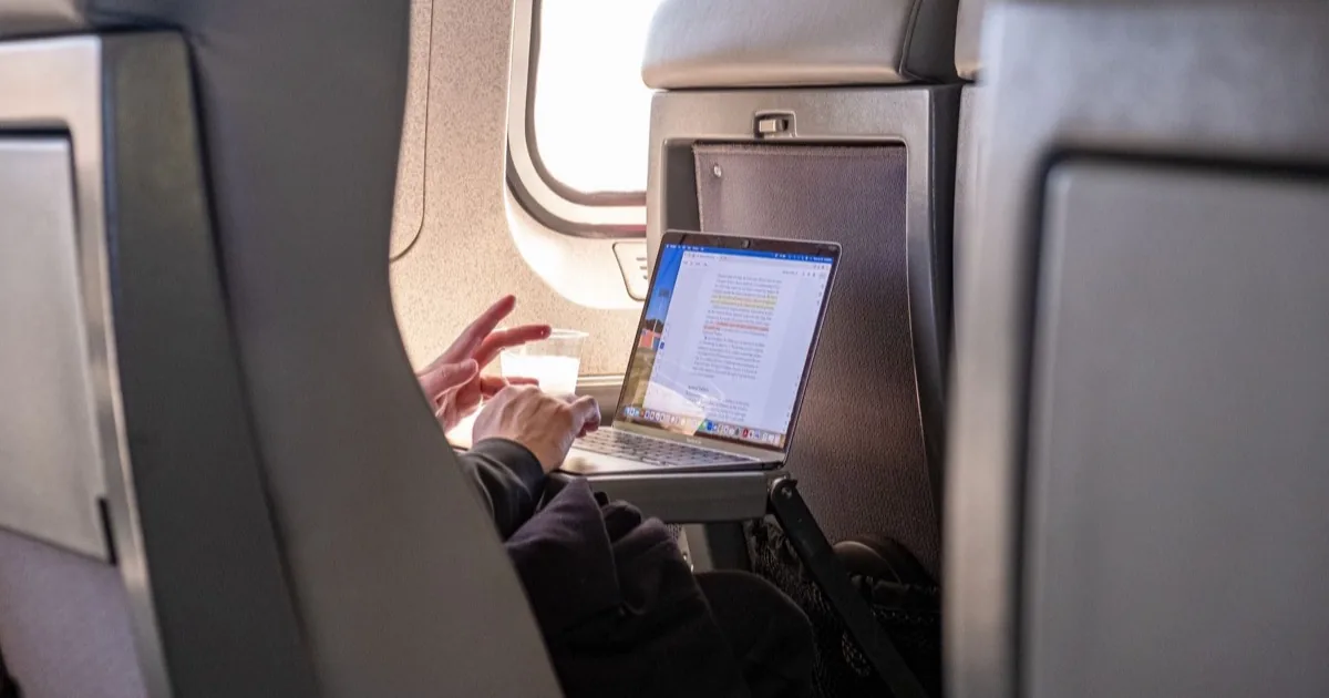 A passenger working on a laptop beside an airplane window.