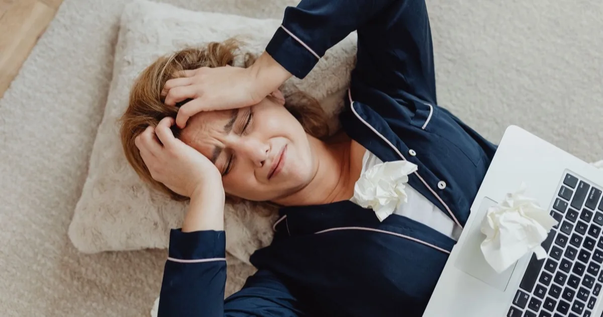 A frustrated woman lying beside her laptop with crumpled notes.